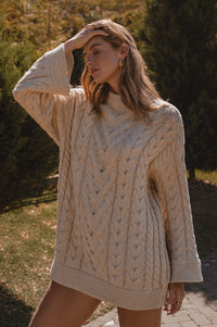 Woman wearing a beige cable knit sweater outdoors