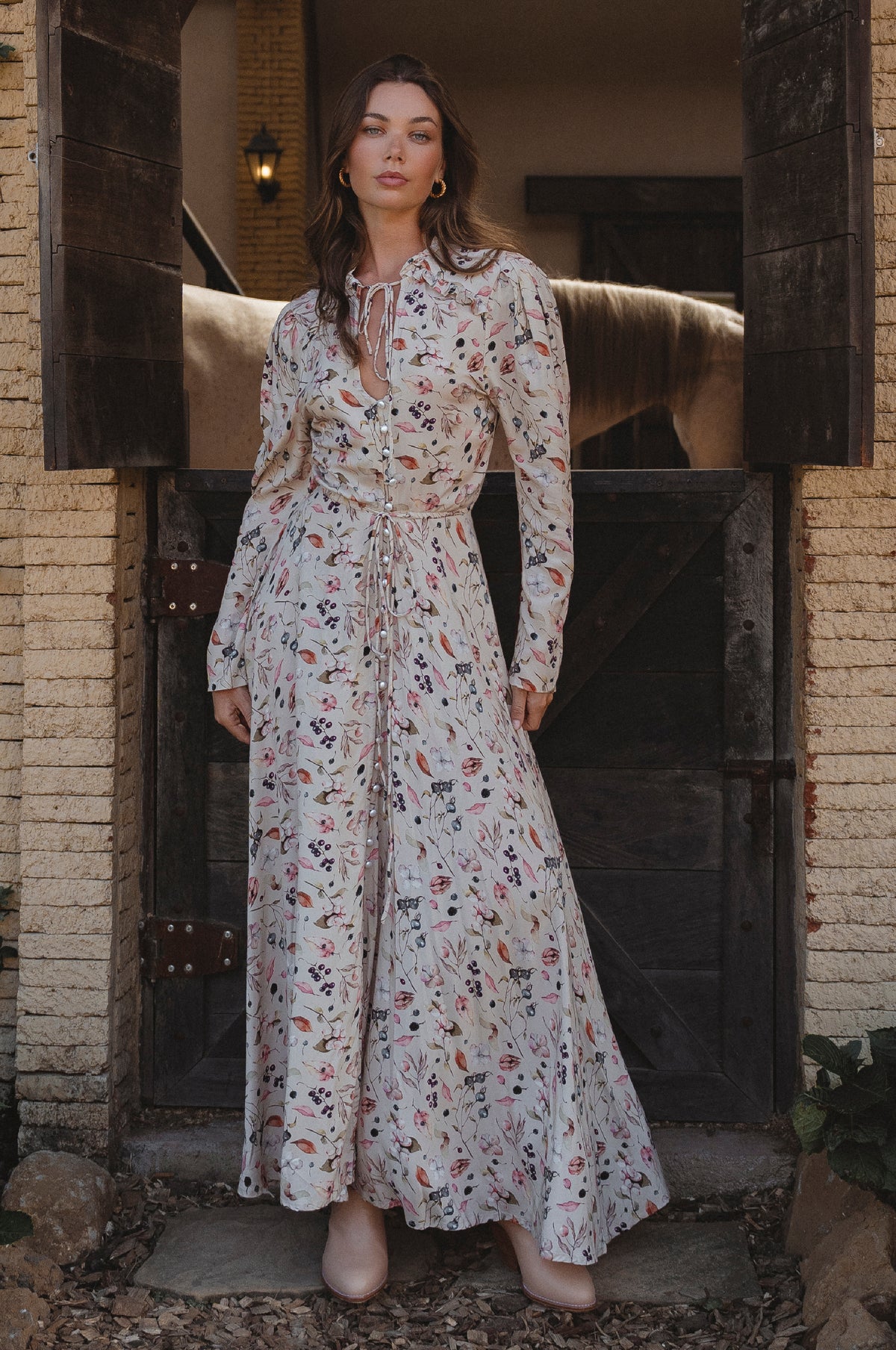 Woman in a floral dress standing in front of a rustic door.