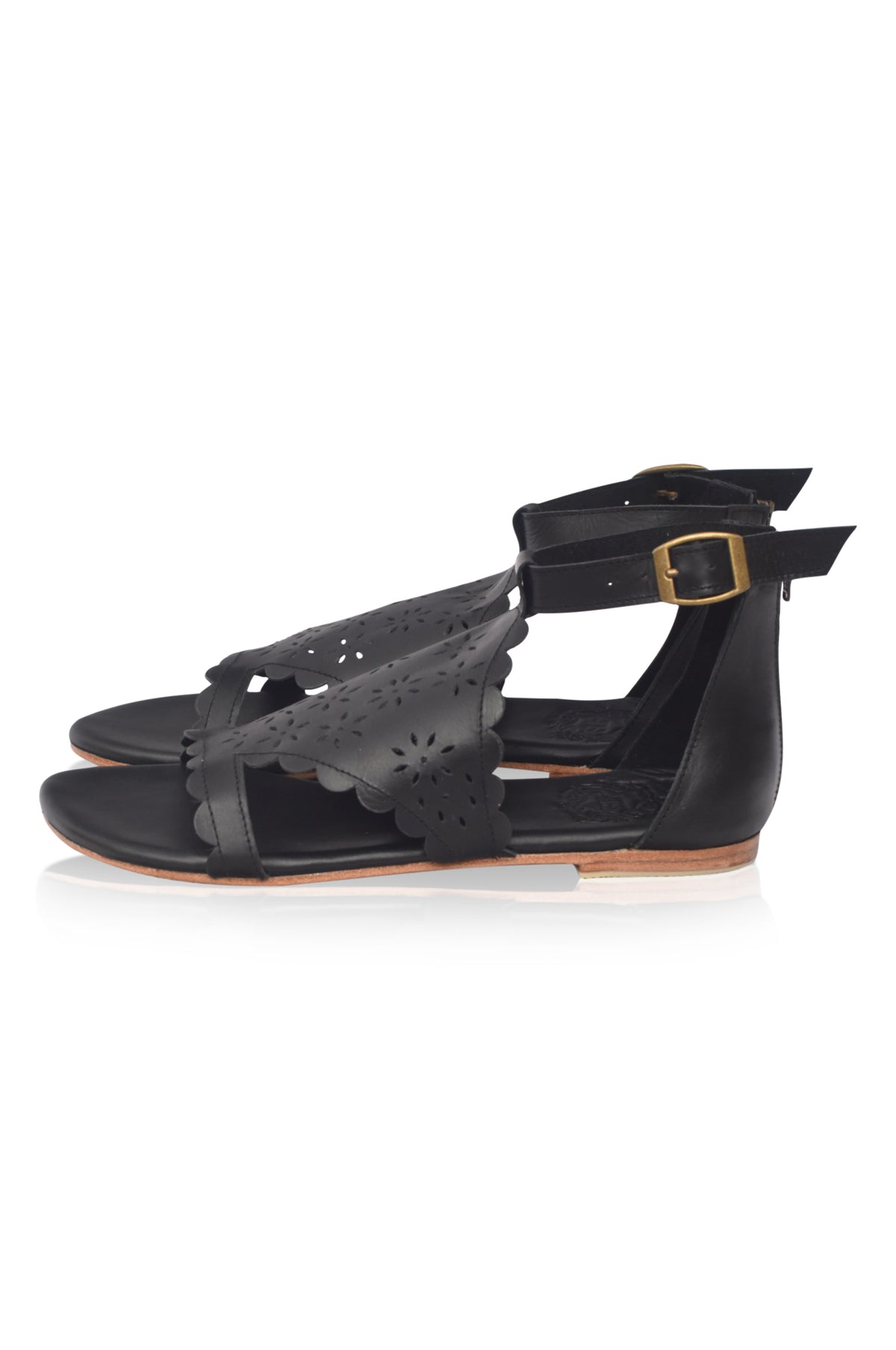 Black leather flat sandals with scalloped cutout straps, an ankle strap with a gold-tone buckle, and a low tan block heel, shown against a plain white background.