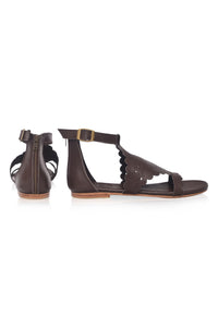 A pair of dark brown leather flat sandals with cutout details, a T-strap design, and an ankle buckle strap, shown from the side and back on a white background.