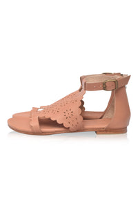 A single women's flat sandal in a warm nude pink color, featuring a scalloped cutout pattern across the T-strap and an adjustable ankle strap with a gold-tone buckle, shown from a side profile on a white background.