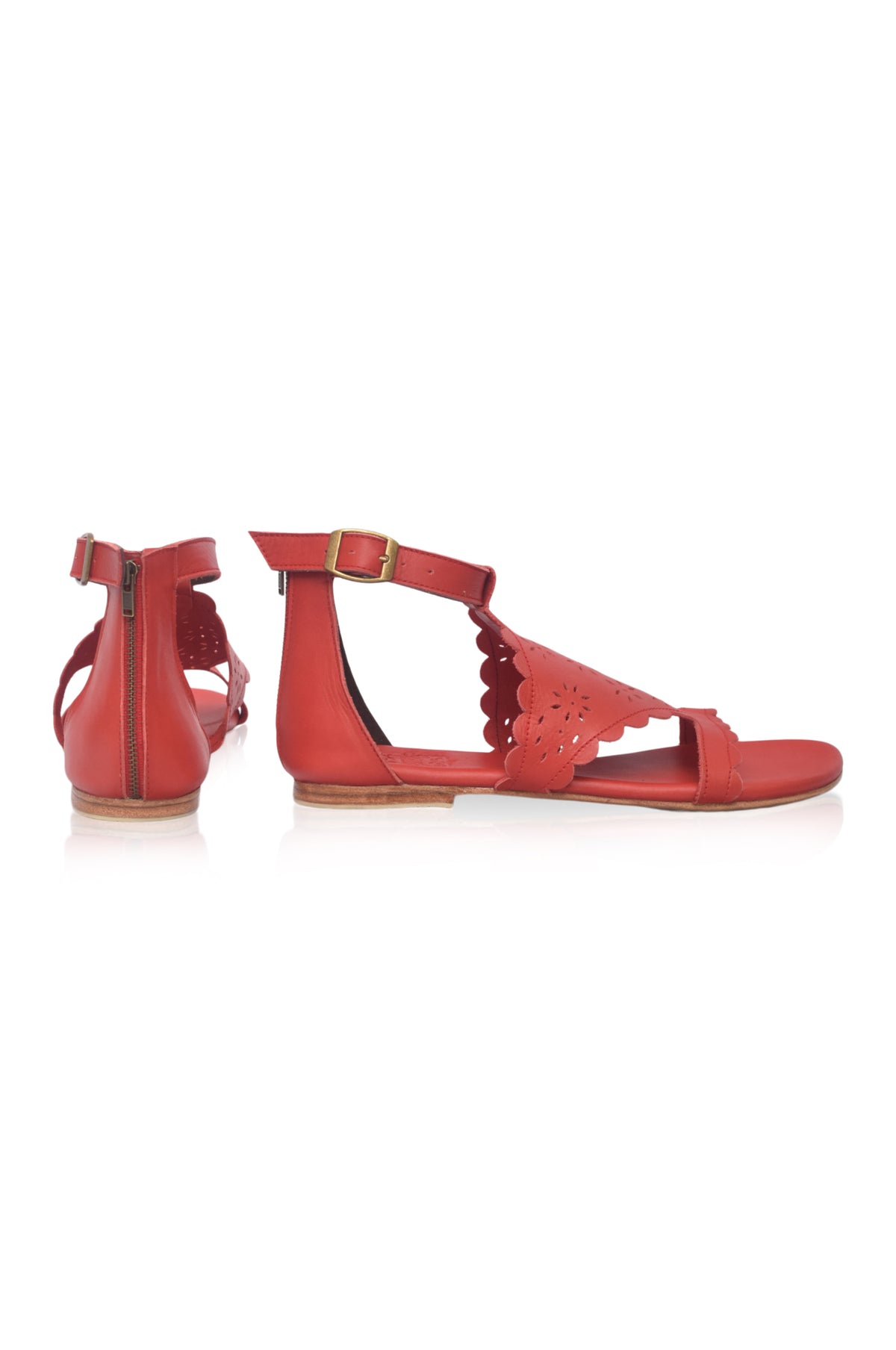 A pair of red flat sandals with cutout details, a scalloped edge, and an adjustable ankle strap with a gold buckle, shown from the side and back on a white background.