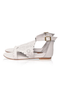 White flat sandals with a scalloped cutout toe strap, an adjustable ankle strap with a gold-tone buckle, and a low block heel, shown from a side profile on a white background.