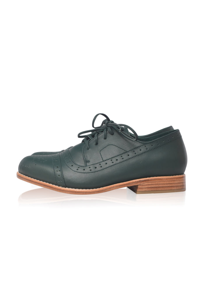 A dark green leather oxford-style shoe with brogue detailing, black laces, and a brown stacked wood heel, shown from a side profile on a white background.