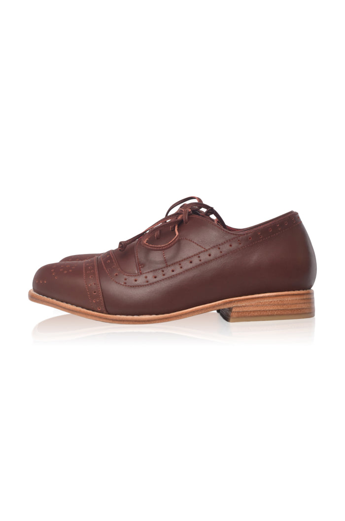 A single dark brown leather wingtip oxford shoe with brogue detailing, shown in a side profile on a white background with a soft reflection.