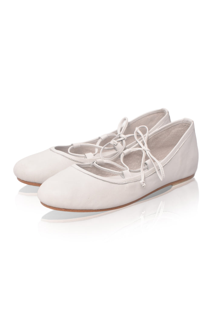 A pair of light beige ballet flats with white laces, shown on a clean white background with a soft reflection.