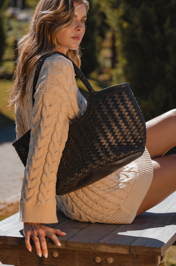 Woman sitting on a bench holding a black woven handbag