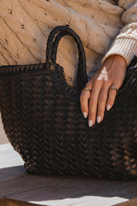 Person holding a woven black handbag with a neutral sweater