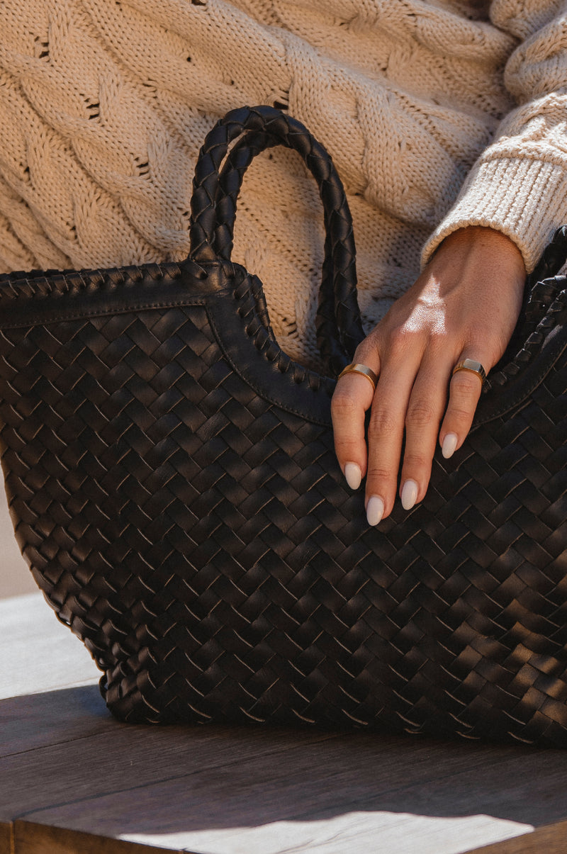Person holding a woven black handbag with a neutral sweater