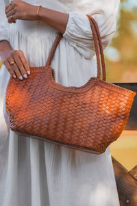 Brown woven handbag held by a person wearing a white dress.