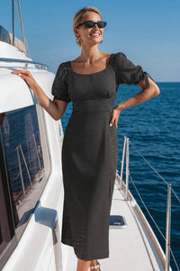 Woman in a black dress standing on a boat with blue water and sky in the background