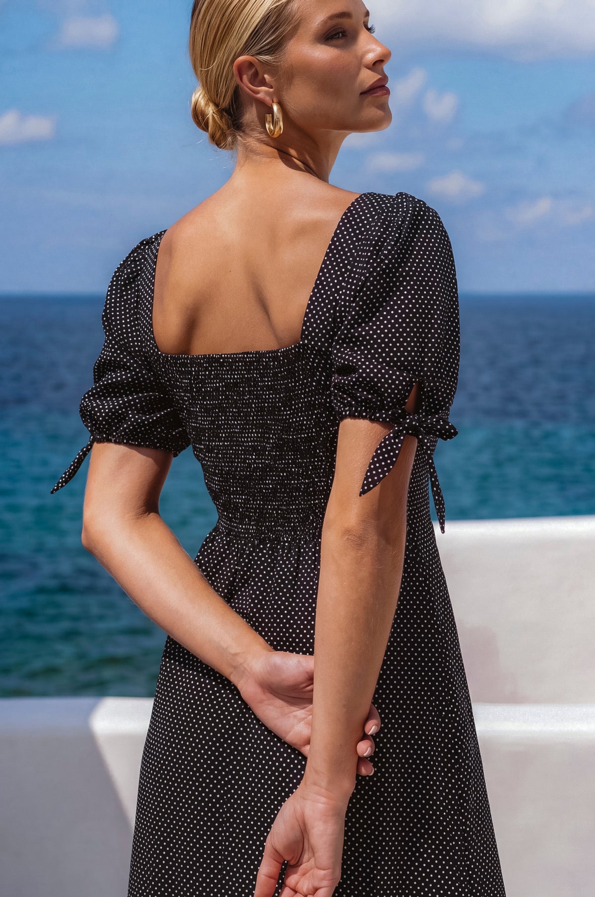 Woman in a black polka dot dress standing by the ocean