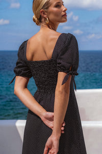 Woman in a black polka dot dress standing by the ocean