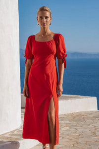 Woman in a red dress standing by a white wall with a blue sky and ocean in the background