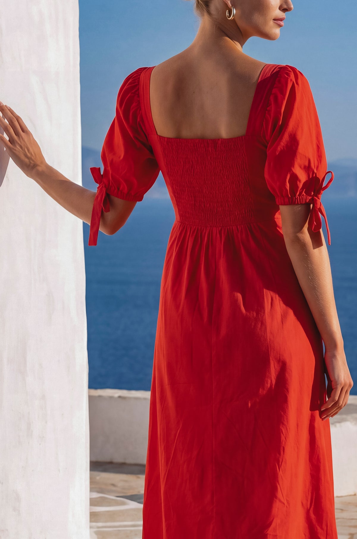 Woman wearing a red dress with a white architectural structure and blue sky in the background