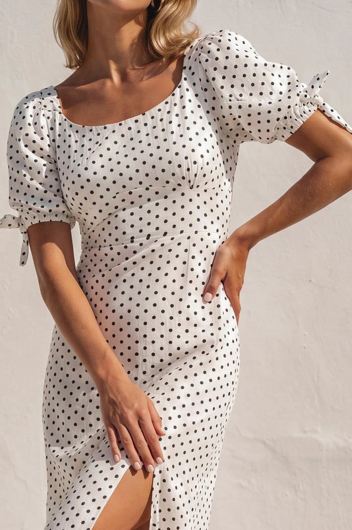 Woman wearing a white dress with black polka dots against a plain background