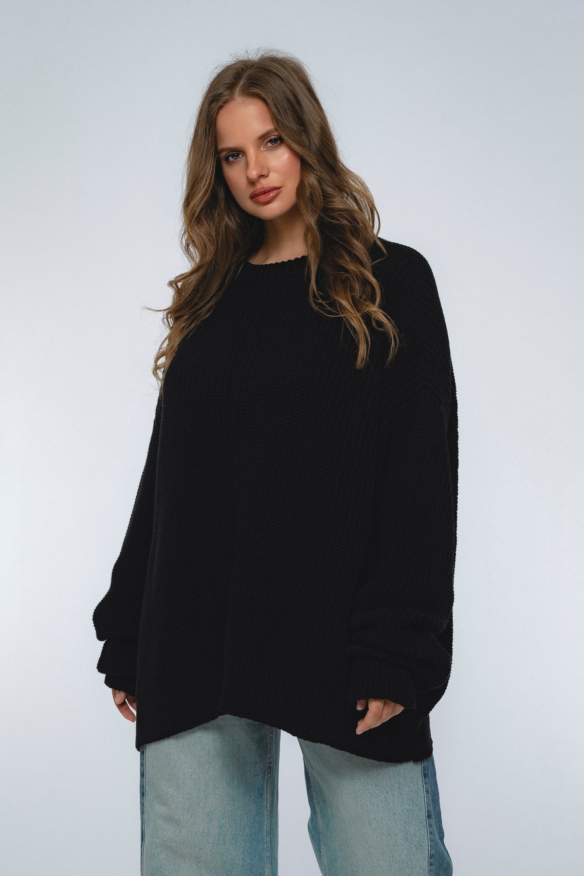 Woman wearing a black sweater and light blue jeans against a white background