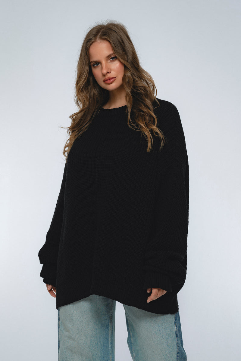 Woman wearing a black sweater and light blue jeans against a white background