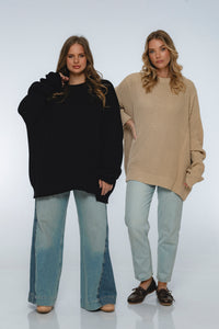Two women wearing oversized sweaters and jeans on a white background