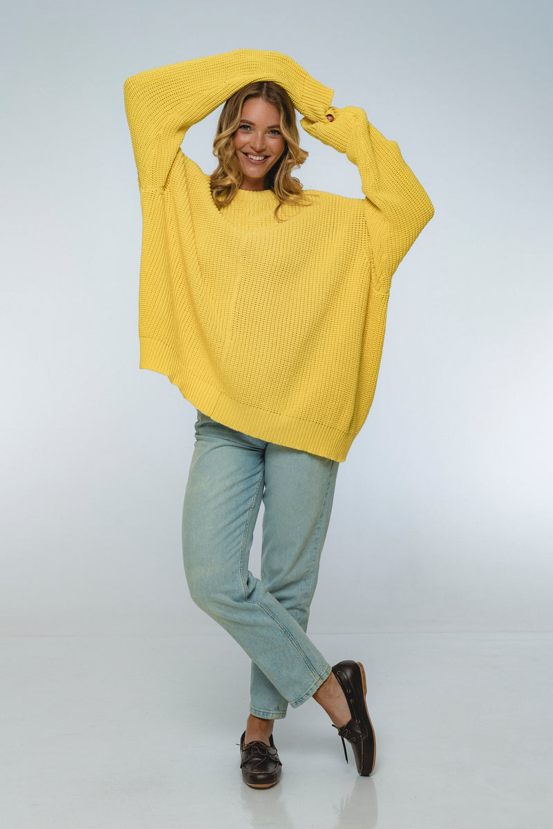 Woman wearing a yellow sweater and light blue pants on a white background
