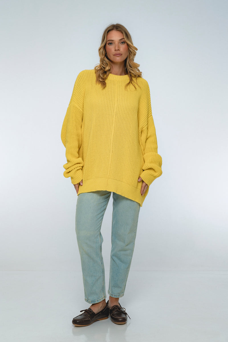 Woman wearing a yellow sweater and light blue jeans on a white background