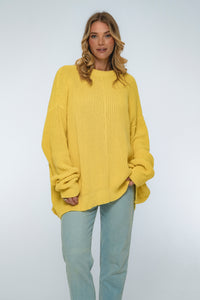 Woman wearing a yellow sweater and light blue jeans on a white background