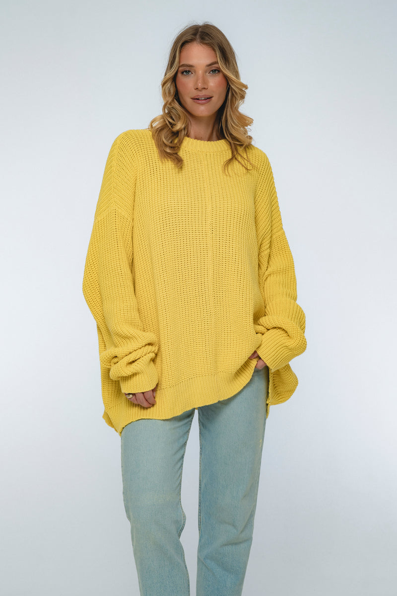 Woman wearing a yellow sweater and light blue jeans on a white background