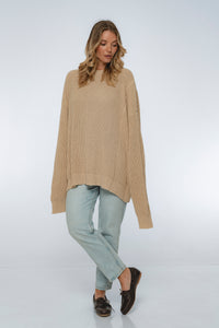 Woman wearing a beige sweater and light blue pants on a white background