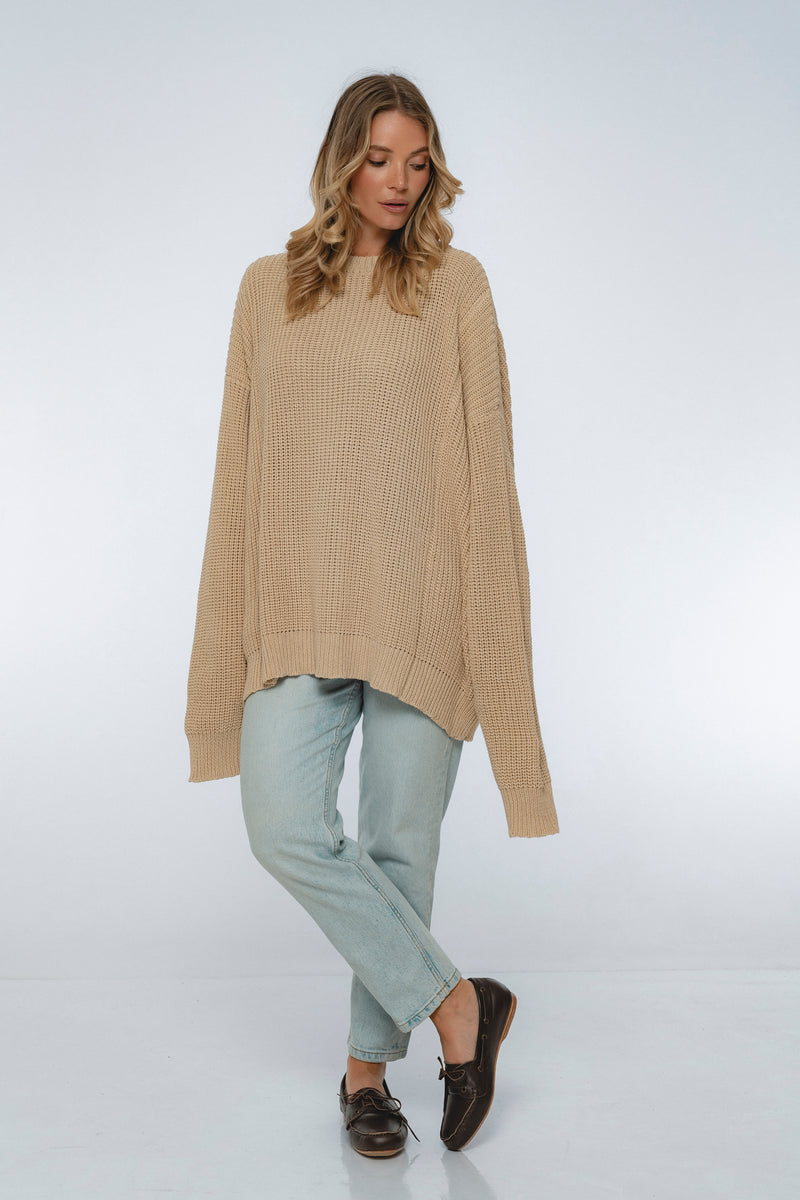 Woman wearing a beige sweater and light blue pants on a white background