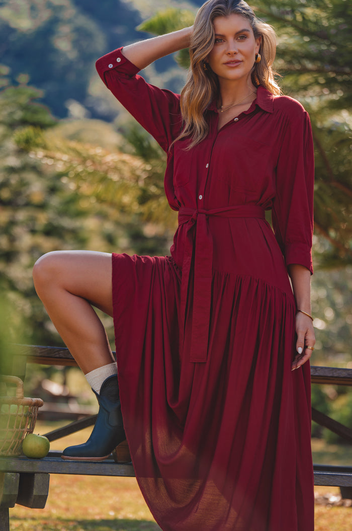 Woman in a red dress sitting outdoors with greenery in the background