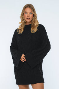 Woman wearing a black cable knit sweater dress against a white background
