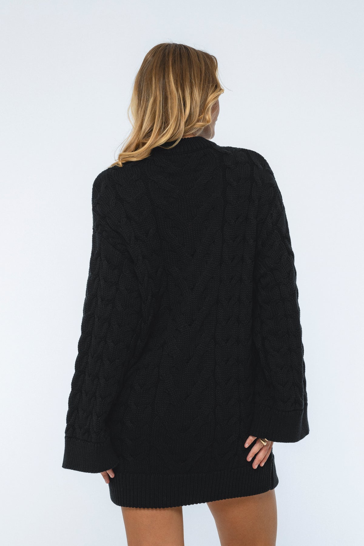 Person wearing a black cable knit sweater on a white background