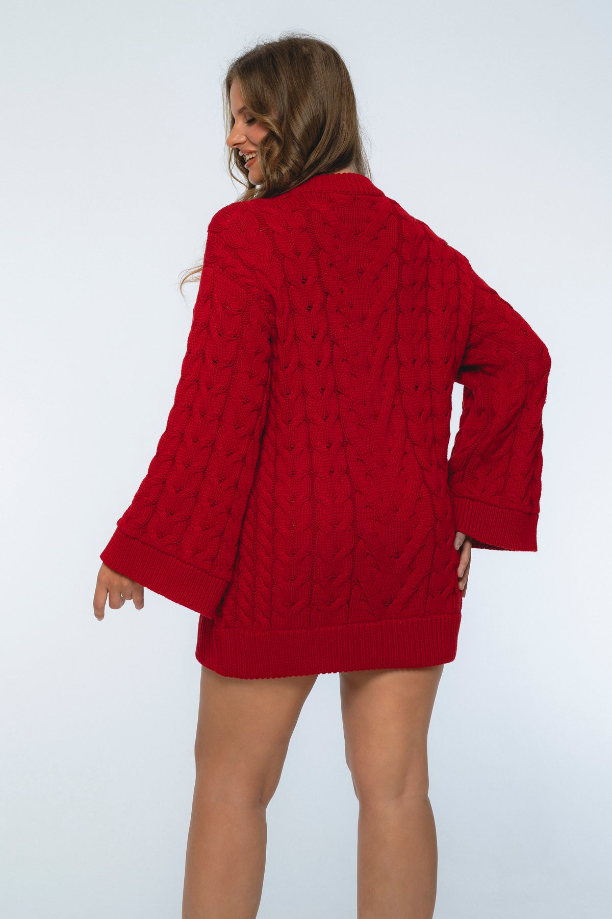 Person wearing a red cable knit sweater on a white background