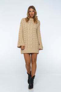 Woman wearing a beige cable knit sweater dress on a white background