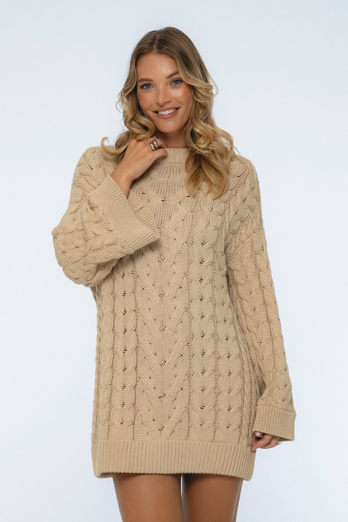 Woman wearing a beige cable knit sweater on a white background