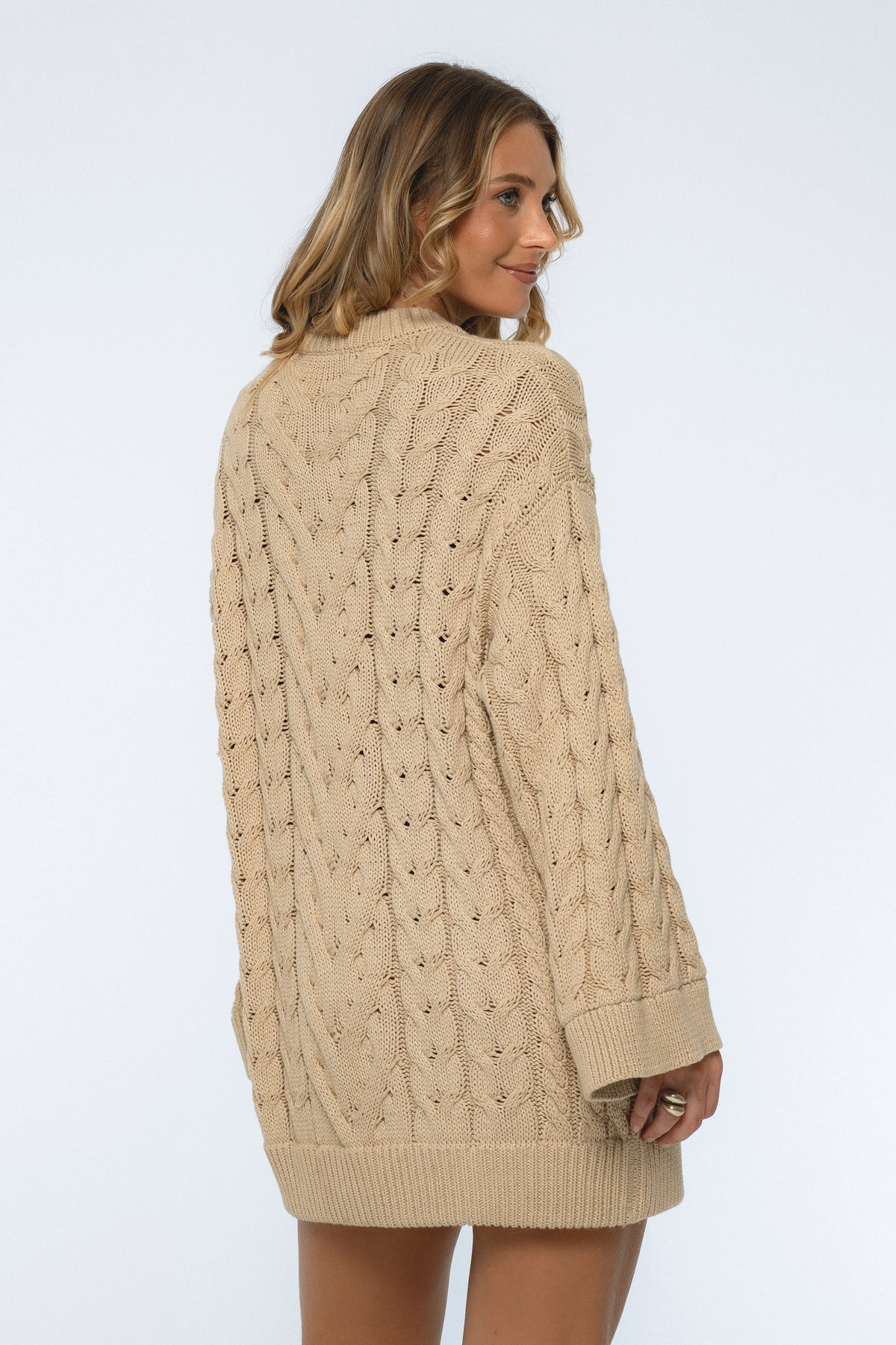 Woman wearing a beige cable knit sweater on a white background