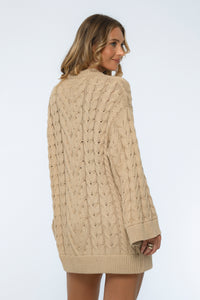 Woman wearing a beige cable knit sweater on a white background