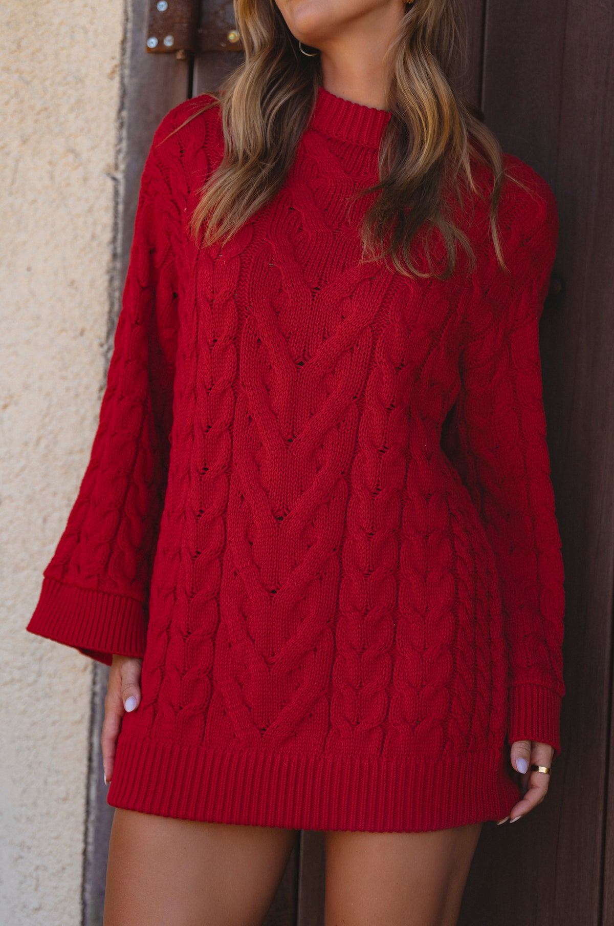 Red cable knit sweater dress worn by a person against a neutral wall.
