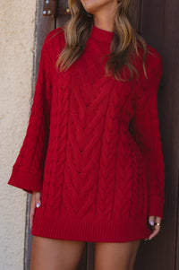 Red cable knit sweater dress worn by a person against a neutral wall.