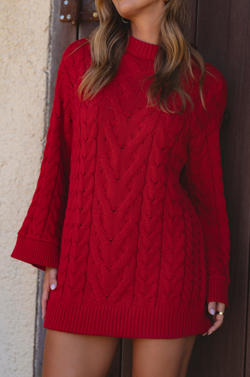 Red cable knit sweater dress worn by a person against a neutral wall.