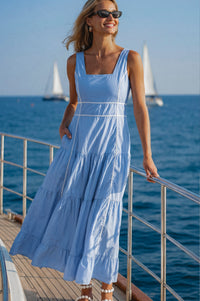 Woman in a light blue dress standing on a boat with sailboats in the background.
