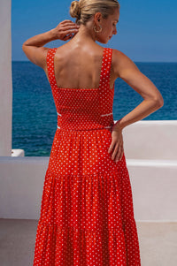 Woman in a red polka dot dress standing by the ocean.