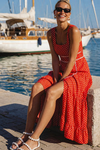 Woman in a red polka dot dress sitting by a harbor with boats in the background.