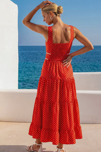 Woman in a red polka dot dress standing by the ocean with white buildings in the background