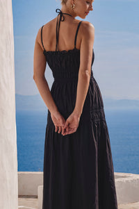 Woman in a black dress standing against a blue sky and ocean backdrop.