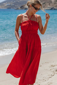 Woman in a red dress standing on a beach with ocean and mountains in the background