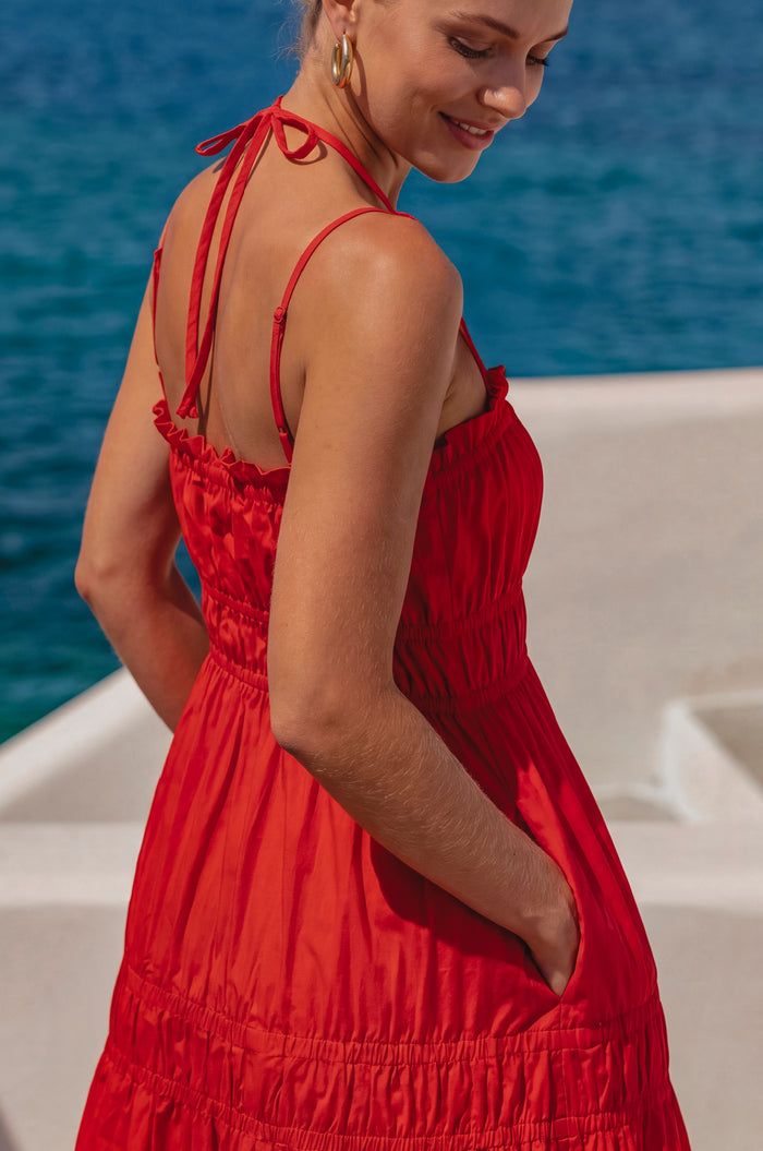 Woman in a red dress standing on a boat with blue water in the background