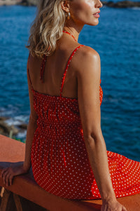 Woman in a red polka dot dress sitting by a blue water body