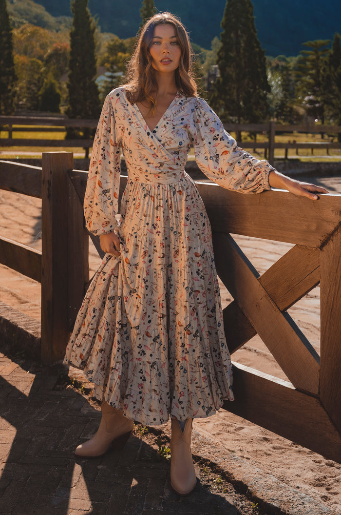 Woman in a floral dress standing by a wooden fence with a scenic background