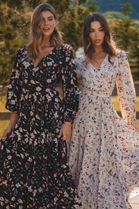 Two women wearing floral dresses standing outdoors with a scenic background.